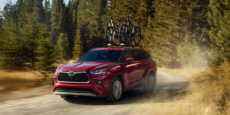 Red Toyota Highlander SUV driving through a forest trail with bicycles mounted on the roof.